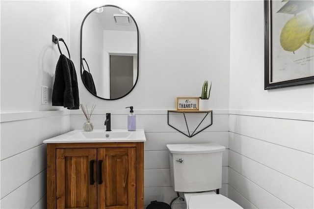 bathroom featuring toilet, vanity, tile walls, and wainscoting