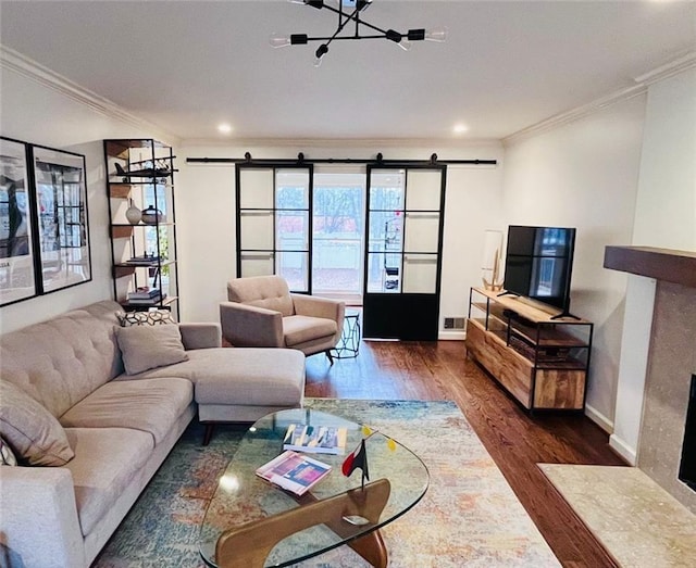 living area with a fireplace with flush hearth, a barn door, wood finished floors, and crown molding