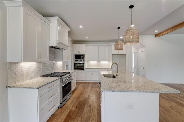 kitchen with a kitchen island with sink, white cabinets, decorative light fixtures, appliances with stainless steel finishes, and light hardwood / wood-style floors