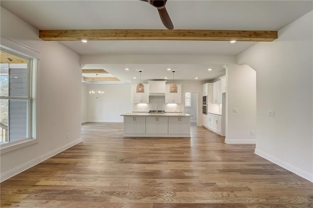 kitchen featuring beam ceiling, a kitchen island with sink, hanging light fixtures, and light wood-type flooring