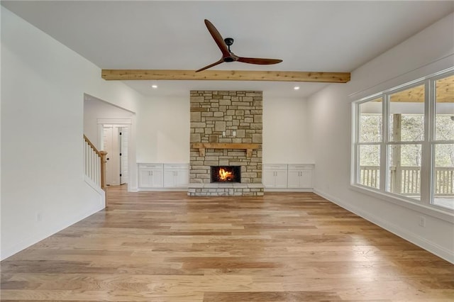 unfurnished living room with beamed ceiling, a stone fireplace, light wood-type flooring, and ceiling fan