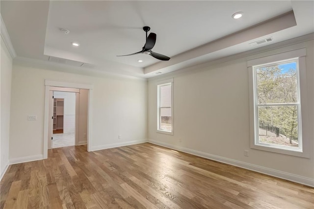 empty room featuring light hardwood / wood-style floors, ceiling fan, and a raised ceiling