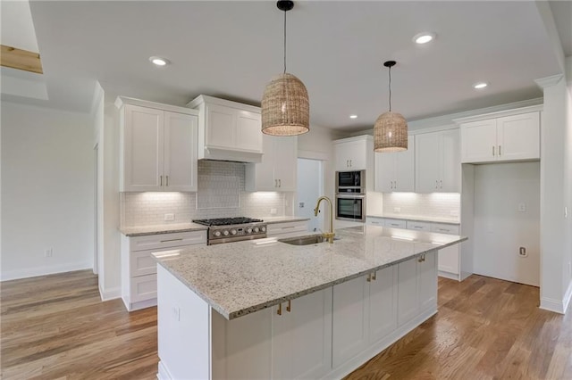 kitchen featuring sink, white cabinets, light wood-type flooring, and an island with sink