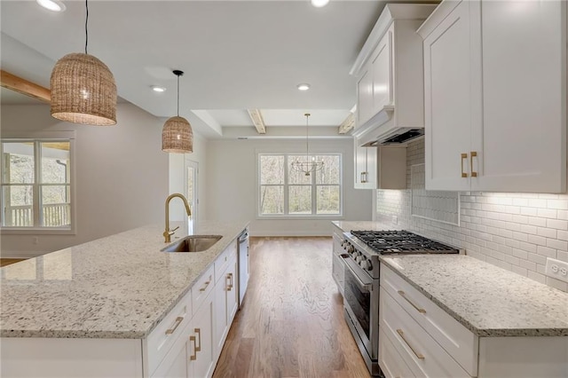 kitchen featuring appliances with stainless steel finishes, sink, white cabinetry, decorative light fixtures, and a kitchen island with sink