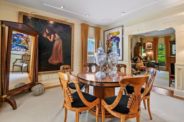 carpeted dining space with ornate columns, ornamental molding, a wainscoted wall, and a decorative wall