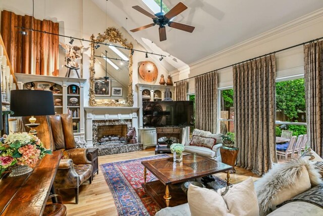 living area featuring crown molding, a fireplace with raised hearth, high vaulted ceiling, a ceiling fan, and wood finished floors