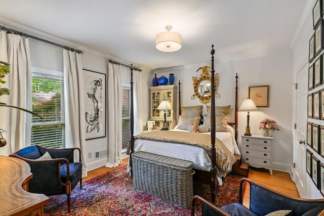 bedroom with visible vents, ornamental molding, baseboards, and wood finished floors