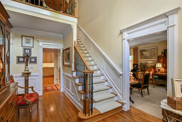 staircase with crown molding, a high ceiling, wainscoting, a decorative wall, and wood finished floors