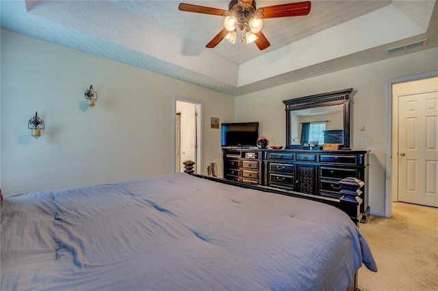 bedroom featuring light carpet, a tray ceiling, visible vents, and a textured ceiling