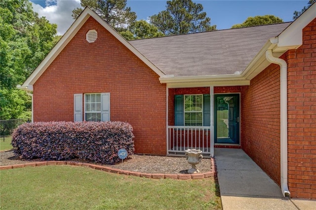 property entrance featuring covered porch, brick siding, roof with shingles, and a lawn