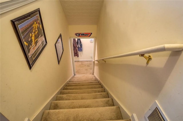 stairway featuring baseboards, visible vents, and a textured ceiling