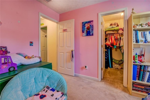 bedroom featuring a closet, a textured ceiling, light carpet, a spacious closet, and baseboards