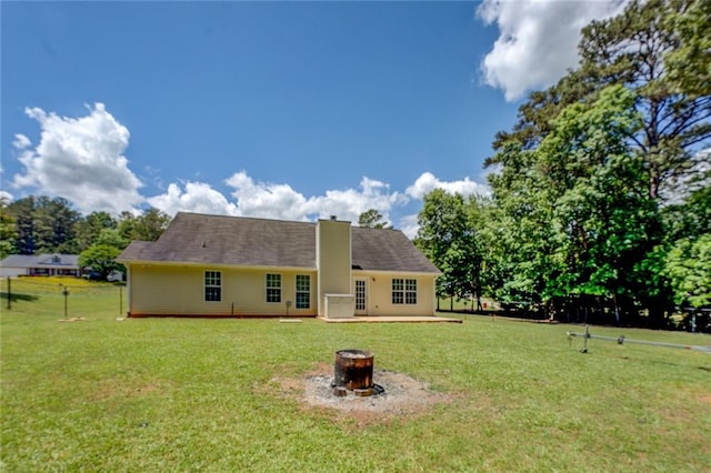 rear view of house with a fire pit, a chimney, and a lawn