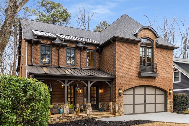 view of front facade featuring driveway, a standing seam roof, a porch, an attached garage, and brick siding