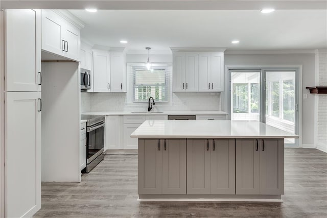 kitchen featuring a sink, appliances with stainless steel finishes, light wood-type flooring, a center island, and crown molding