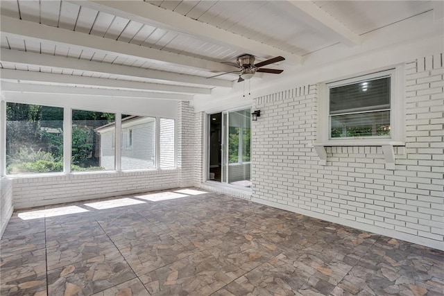 spare room featuring brick wall, stone flooring, a ceiling fan, and beamed ceiling