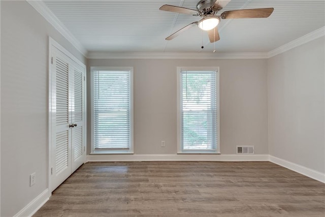 empty room with visible vents, crown molding, baseboards, and wood finished floors