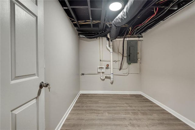 unfinished basement featuring wood finished floors, electric panel, and baseboards