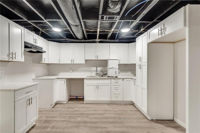 kitchen with white cabinets, light countertops, light wood-type flooring, under cabinet range hood, and a sink