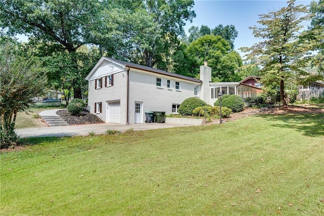 back of house with driveway, a yard, a chimney, and an attached garage