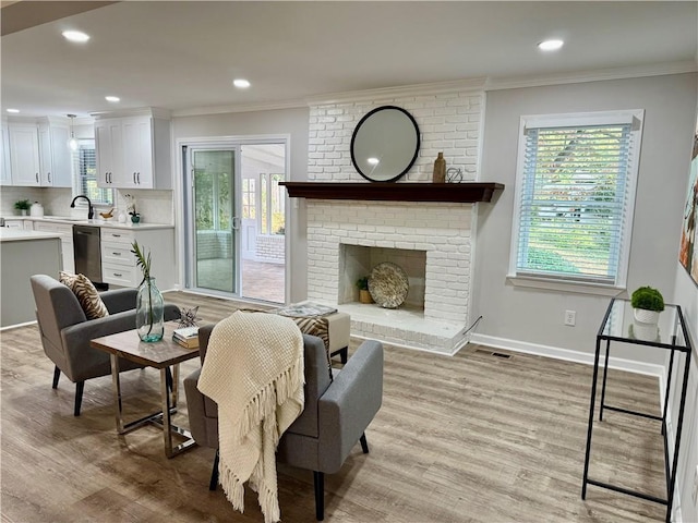 living room featuring ornamental molding, a brick fireplace, light wood-style flooring, and baseboards