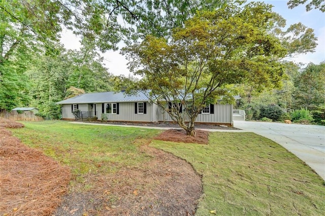 ranch-style home featuring concrete driveway, board and batten siding, fence, metal roof, and a front lawn