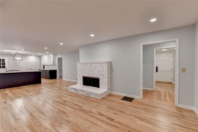 unfurnished living room featuring recessed lighting, a brick fireplace, visible vents, and light wood-style floors