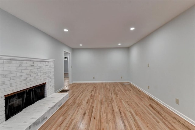 unfurnished living room with light wood finished floors, a brick fireplace, recessed lighting, and baseboards