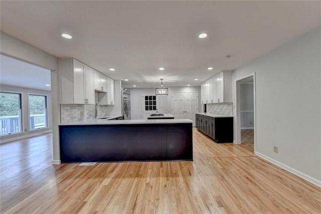 kitchen featuring a peninsula, white cabinetry, baseboards, light countertops, and light wood finished floors