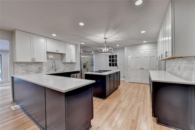 kitchen featuring light stone counters, stainless steel appliances, white cabinetry, a center island, and light wood finished floors