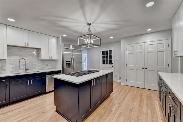 kitchen featuring a sink, white cabinets, appliances with stainless steel finishes, backsplash, and light wood finished floors