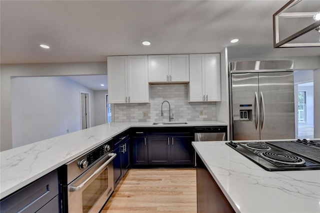 kitchen featuring light stone counters, a sink, white cabinets, appliances with stainless steel finishes, and light wood finished floors