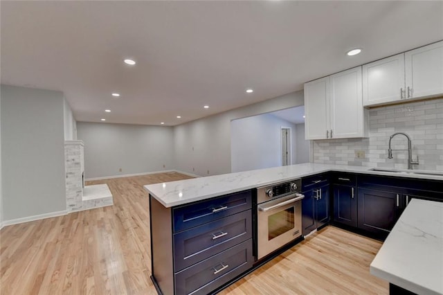 kitchen with light stone counters, white cabinetry, stainless steel oven, a sink, and a peninsula