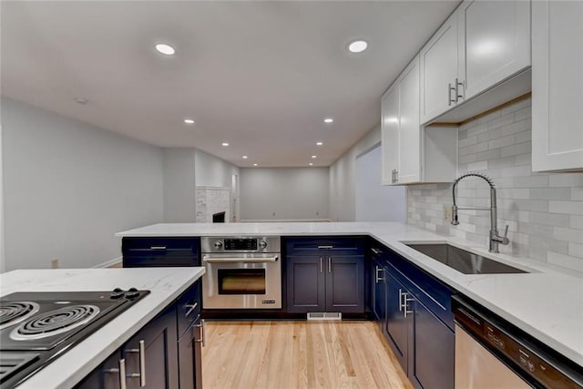 kitchen with stainless steel appliances, light wood-style flooring, white cabinets, a sink, and a peninsula