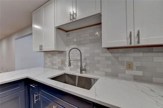 kitchen with tasteful backsplash, white cabinetry, light stone counters, and a sink