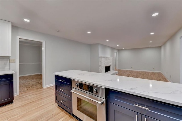 kitchen featuring light stone counters, a fireplace, stainless steel oven, and light wood-style floors