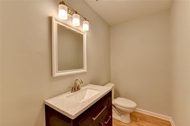 half bath featuring toilet, baseboards, wood finished floors, and vanity