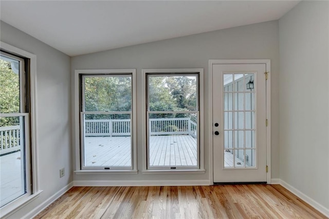 doorway with plenty of natural light, vaulted ceiling, light wood-style flooring, and baseboards