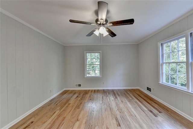 empty room featuring light wood-style floors, visible vents, crown molding, and baseboards