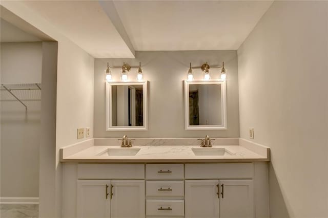 bathroom featuring double vanity, a spacious closet, a sink, and baseboards