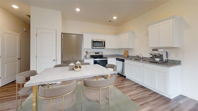 kitchen with appliances with stainless steel finishes, light wood-type flooring, a sink, and white cabinetry