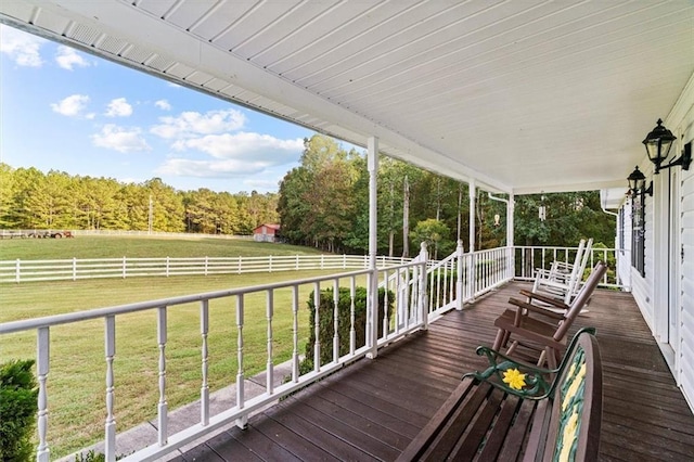 wooden terrace with a rural view, a porch, a lawn, and fence