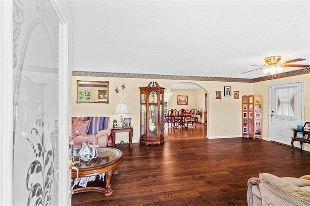 living room with arched walkways, a ceiling fan, a textured ceiling, wood finished floors, and baseboards