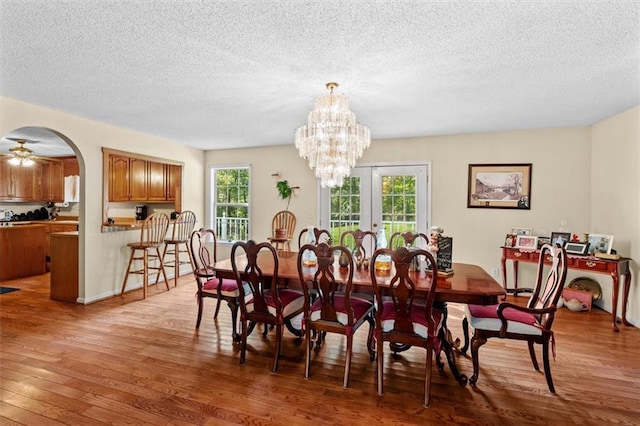 dining room with arched walkways, french doors, light wood-style flooring, a textured ceiling, and ceiling fan with notable chandelier