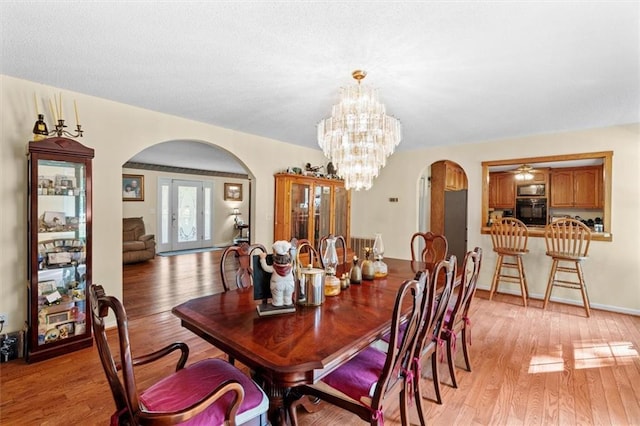 dining room with arched walkways, light wood-type flooring, and a notable chandelier