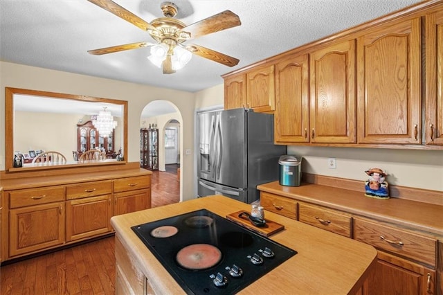 kitchen with arched walkways, dark wood-style flooring, stainless steel refrigerator with ice dispenser, brown cabinetry, and black electric cooktop