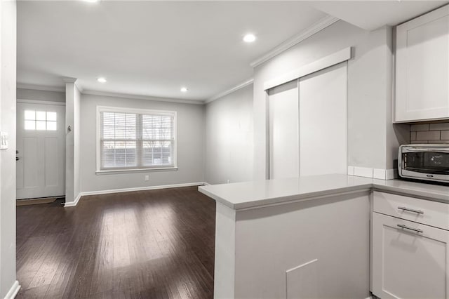 kitchen with crown molding, dark wood-type flooring, kitchen peninsula, and white cabinets