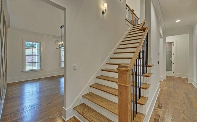 staircase with a chandelier, wood-type flooring, and ornamental molding