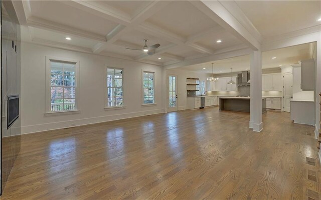 unfurnished living room featuring hardwood / wood-style floors, coffered ceiling, ceiling fan with notable chandelier, crown molding, and beam ceiling