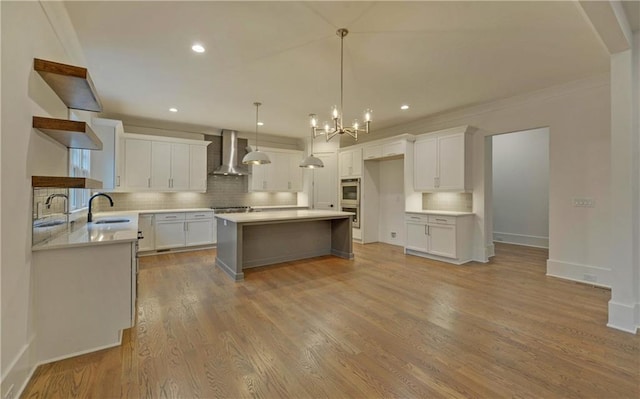 kitchen with white cabinetry, wall chimney exhaust hood, hanging light fixtures, light hardwood / wood-style flooring, and a kitchen island